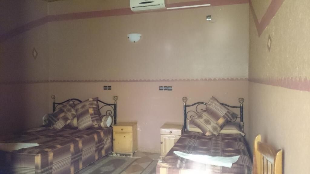 Une chambre avec deux lits, chacun doté d’une tête de lit et d’une table de chevet. On y trouve un luminaire au plafond et une applique murale.