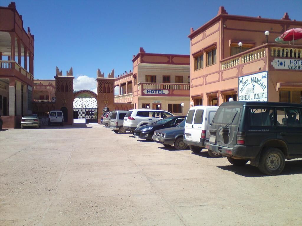 A hotel with a signboard, a parking lot with several cars, and a building with a balcony.