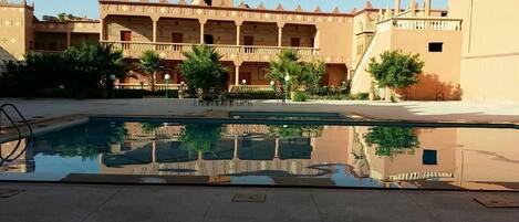 A swimming pool with a reflection of a building with multiple balconies and columns.