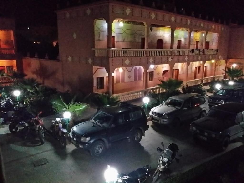 A multi-story building with balconies and a parking area with several cars and motorcycles.