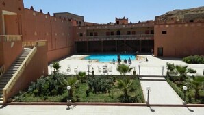 Ein Innenhof mit Swimmingpool, Palmen und einer Treppe, die zu einer erhöhten Ebene führt.