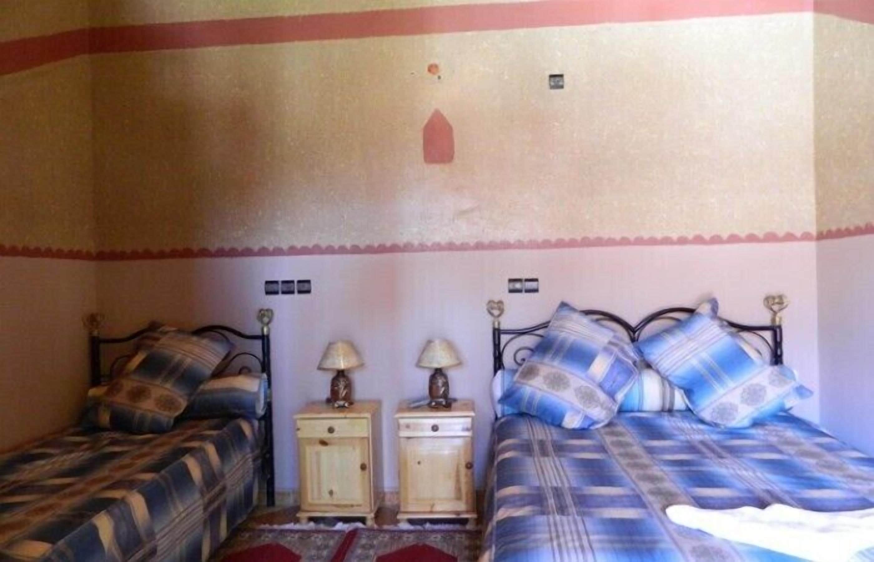 Une chambre avec deux lits, chacun recouvert d’une couvre-lit à motifs différents, deux tables de chevet avec des lampes et un motif décoratif sur le mur.