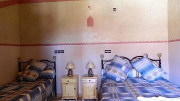 Une chambre avec deux lits, chacun recouvert d’une couvre-lit à motifs différents, deux tables de chevet avec des lampes et un motif décoratif sur le mur.