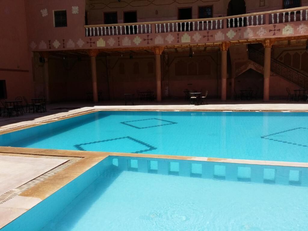 A swimming pool with a tiled deck area, surrounded by a building with a balcony and columns.