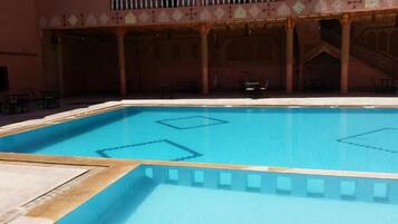 A swimming pool with a tiled deck area, surrounded by a building with a balcony and columns.