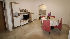 A compact living space with a dining area, kitchenette, and a TV on a wooden stand. - Villa Nino (Liznjan)