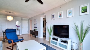 A modern living room with a blue armchair, a white coffee table, a flat-screen TV on a white stand, and a large plant. - Dolphin Cove  PH 9 '90 day min stay with 2 week lead time' (Clearwater Beach)