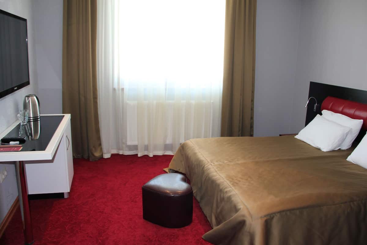 A hotel room with a bed, a desk, a chair, a TV, and a window with curtains.