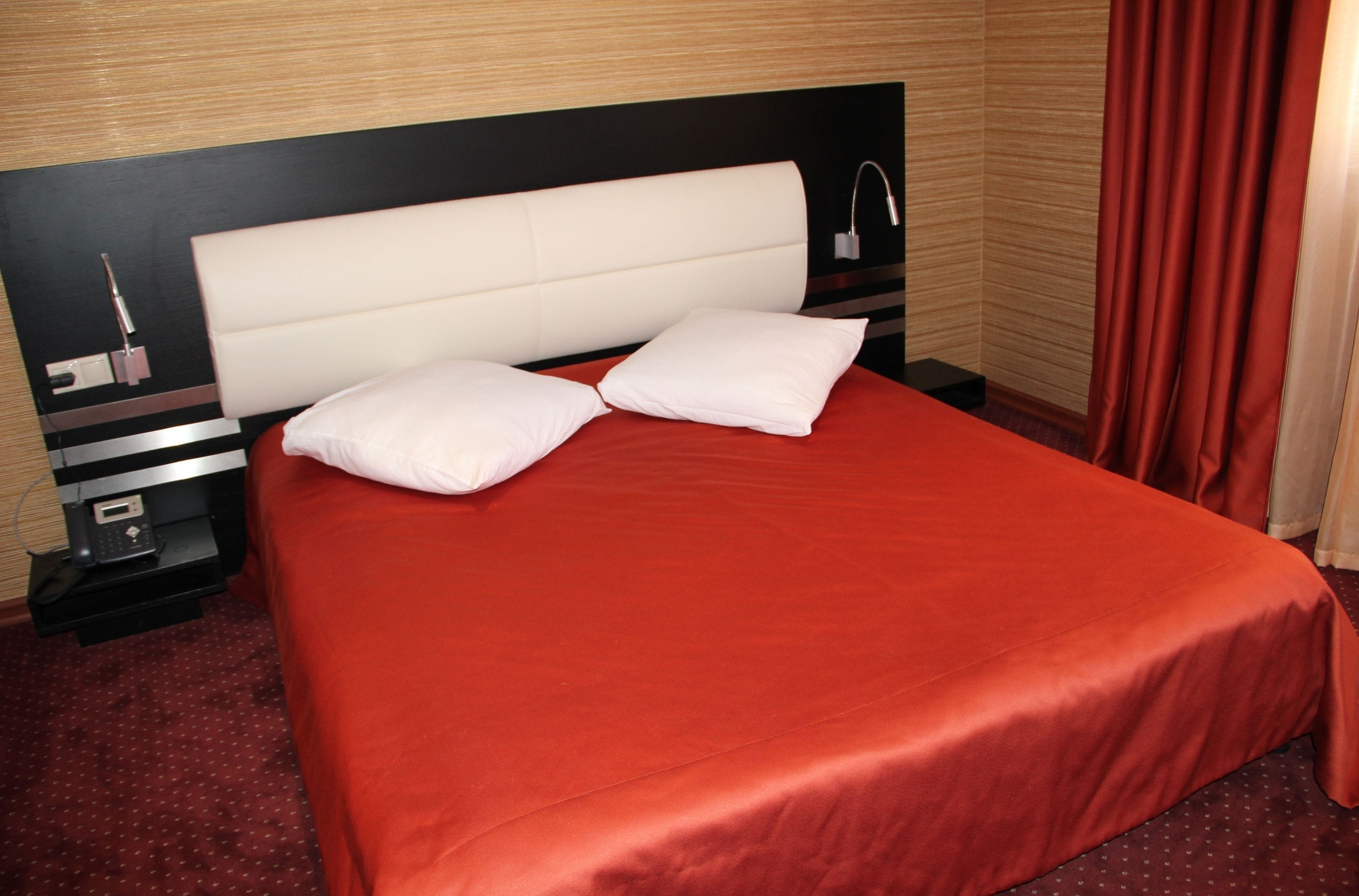 A hotel room with a bed, two pillows, a nightstand, and a lamp.