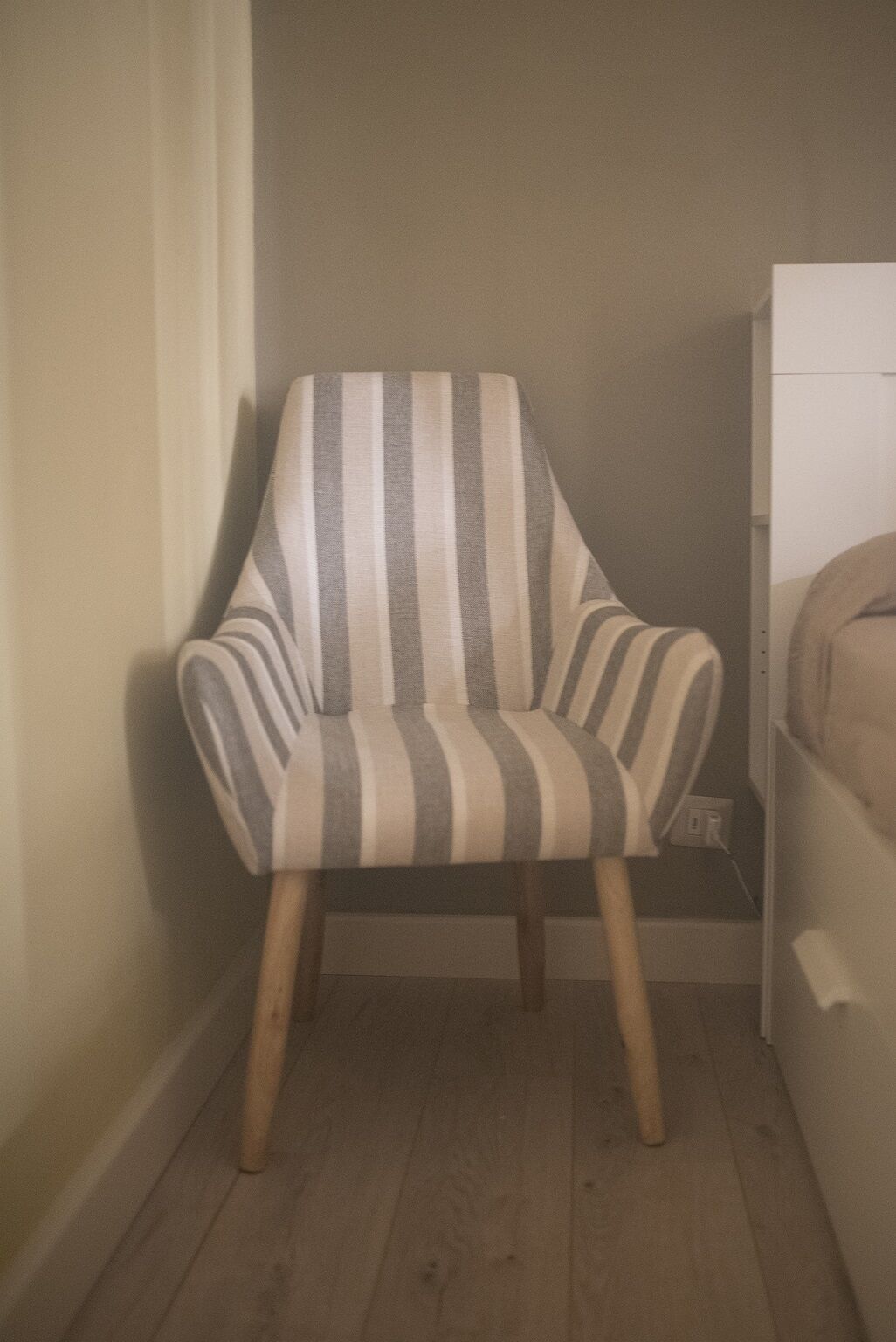 A corner armchair with striped upholstery, wooden legs, and a visible electrical outlet on the wall.