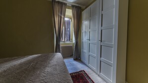 Een slaapkamer met een bed, een raam met gordijnen, een radiator en een kledingkast.