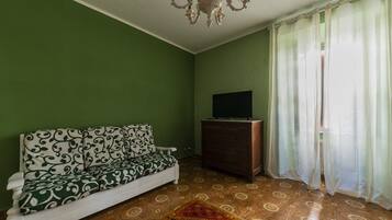 Una habitación con sofá, televisor sobre un mueble de madera, candelabro y suelo estampado.