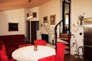 Een woonkamer met een rode bank, een eettafel met een wit tafelkleed, en een trap die naar een verdieping leidt.