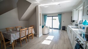Een moderne keuken met witte kasten, een eethoek met houten stoelen en een tafel, en een groot raam met gordijnen.