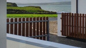 Uitzicht vanuit een raam op een grasrijke omgeving met een houten omheining en een gebouw met een witte gevel en donker dak.
