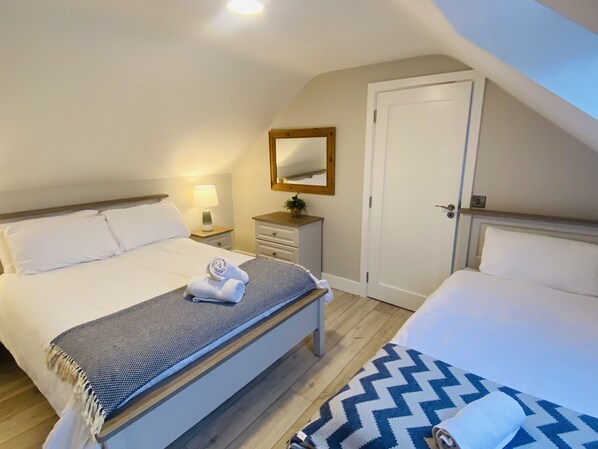 Une chambre avec deux lits, une table de chevet avec une lampe, un miroir et une porte.