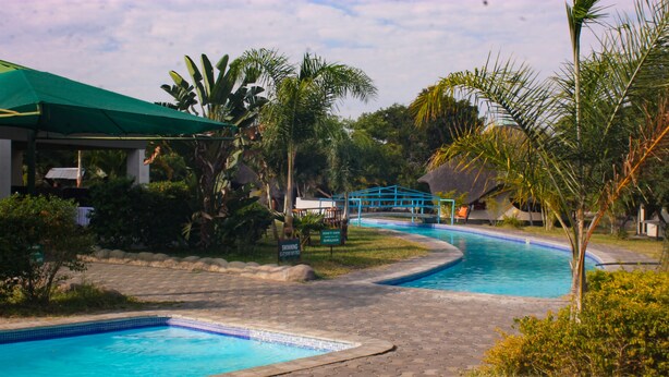 Zona de piscina con área de descanso cubierta, piscina azul y exuberante vegetación tropical.