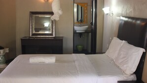 Una habitación de hotel con cama, mesita de noche, espejo, lavabo y un tazón verde.