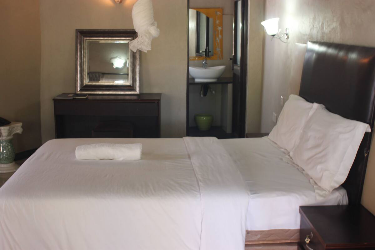Een hotelkamer met een bed, nachtkastje, spiegel, wastafel en een groene kom.