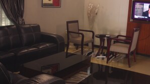 Una sala de estar con un sofá de cuero negro, una mesa de centro de madera, una pequeña mesa redonda con una silla y un televisor montado en la pared.