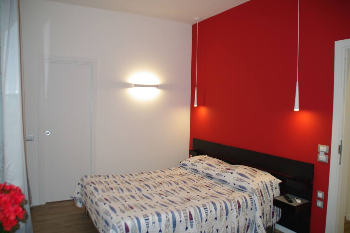 Un dormitorio con cama, mesita de noche, lámpara de pared y una puerta.