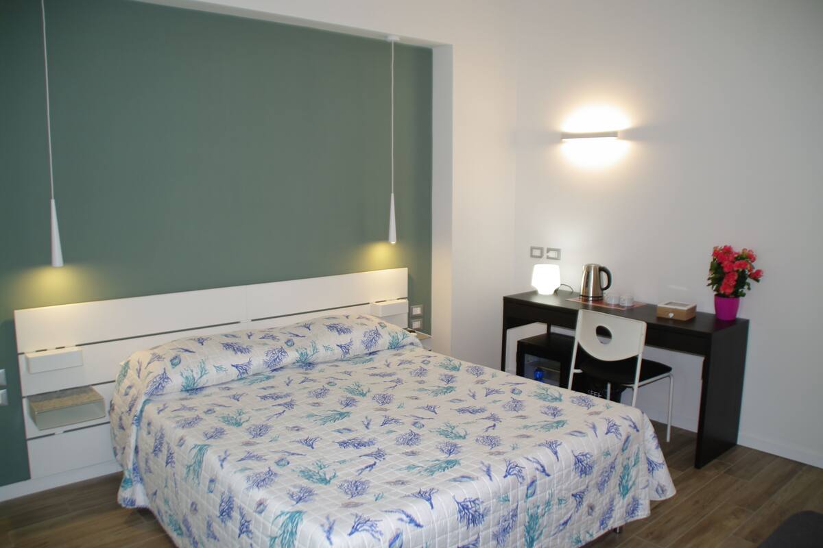 Un dormitorio con una cama, un escritorio y una silla. Hay una lámpara de pared sobre el escritorio.