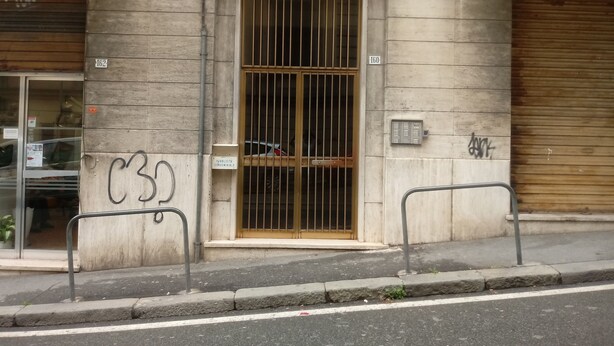 Eine Gebäudefassade mit einer verschlossenen Eingangstür, einer gut sichtbaren Hausnummer und einem Schild, das ein öffentliches Apartmenthaus kennzeichnet.