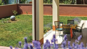 A patio area with a table and chairs, a small garden with grass and flowers, and a large decorative sphere. - Apartman Snježana (Pula)