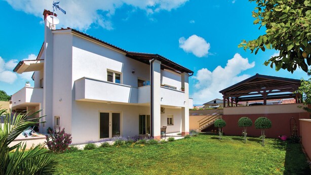 A two-story house with a balcony, a covered patio, and a well-maintained lawn. - Apartman Snježana (Pula)