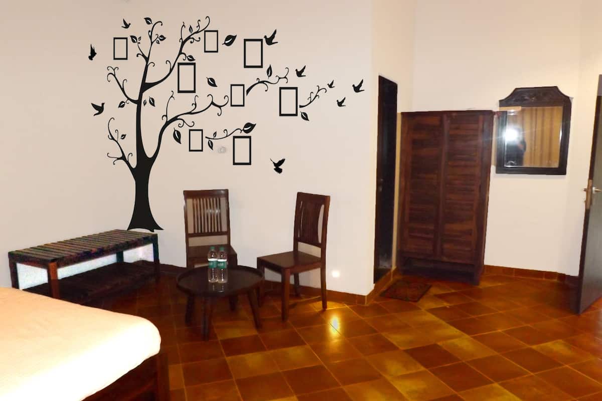 A room with a checkered floor, a bed, two chairs, a small table with water bottles, and a wall decal of a tree with leaves and birds.