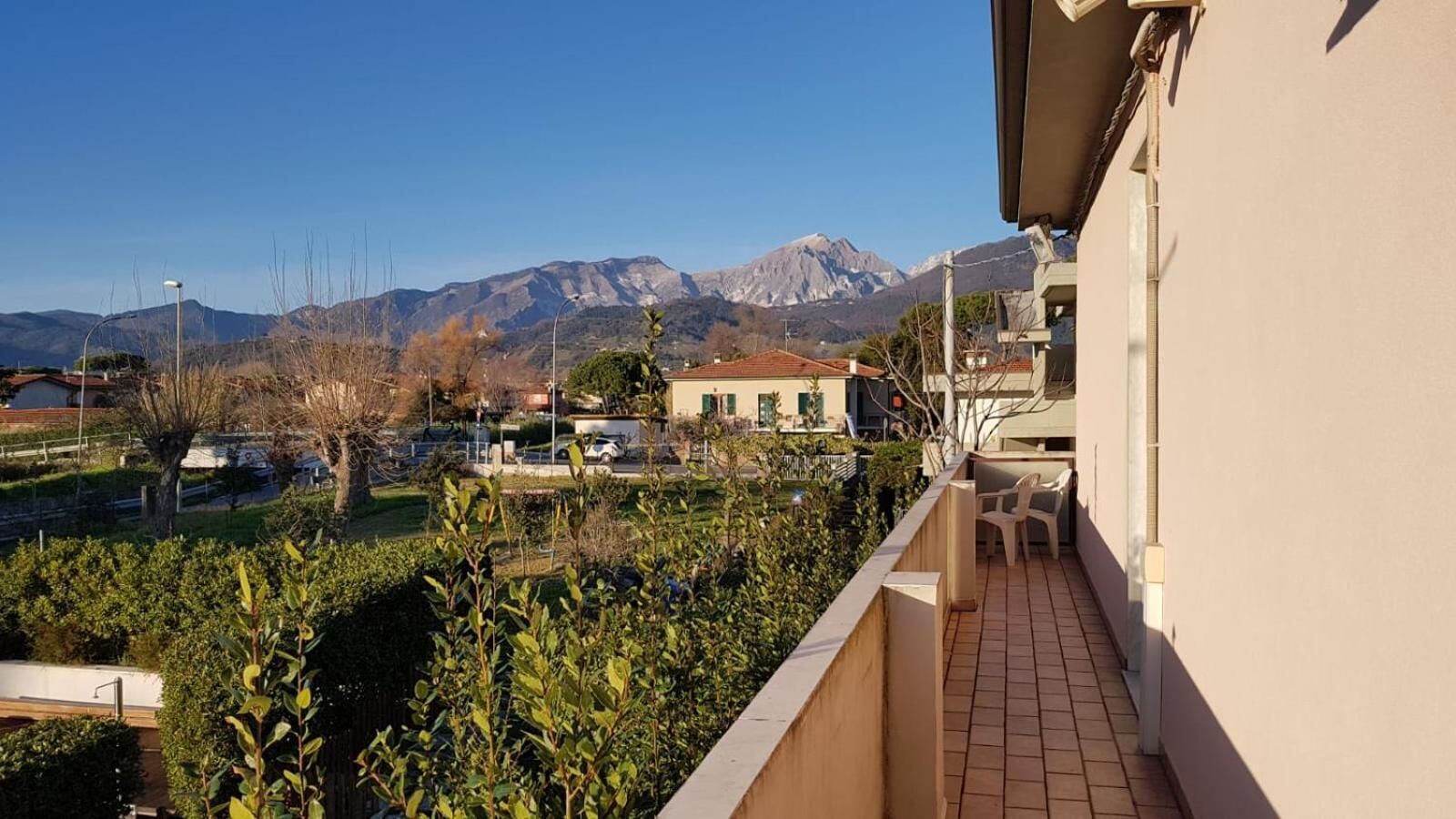 Un balcone con vista sulle montagne, un'area parcheggio e un edificio con pavimento piastrellato.