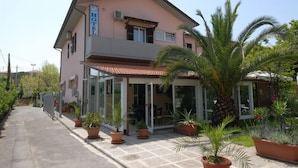 Un hôtel de deux étages avec une façade rose, une entrée couverte et des plantes en pot à l’avant.