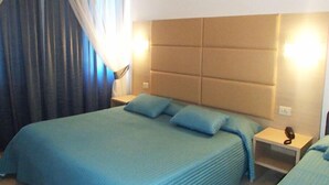 Une chambre d’hôtel avec un grand lit, une tête de lit dotée d’un éclairage intégré, une table de chevet avec une lampe et une fenêtre avec des rideaux.