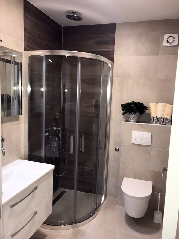 Une salle de bain moderne avec une douche à parois de verre, des toilettes blanches et un meuble-lavabo avec des tiroirs.
