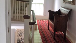 A staircase with a wooden handrail and a red carpet leading to a room with a chair and a framed picture on the wall. - 2 Bedroom Private Apt. in 1825 Whaler's Home on Duck Creek (Wellfleet)