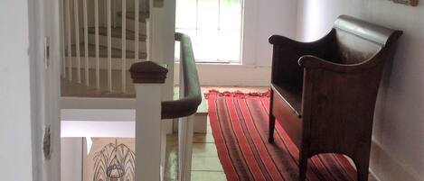 A staircase with a wooden handrail and a red carpet leading to a room with a chair and a framed picture on the wall.