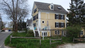 A two-story yellow house with a front porch, a small deck, and a staircase leading to the second floor. - 2 Bedroom Private Apt. in 1825 Whaler's Home on Duck Creek (Wellfleet)