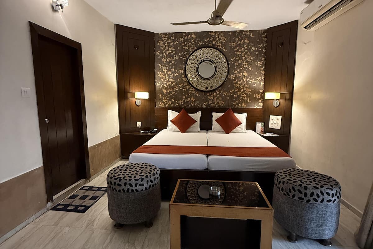 A bedroom with a bed, two ottomans, a coffee table, a ceiling fan, and wall-mounted lights.