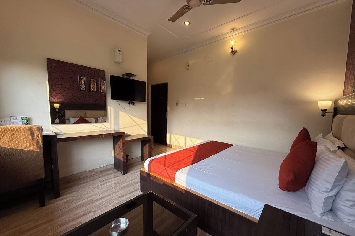 A hotel room with a bed, a desk, a chair, a television, and a ceiling fan.