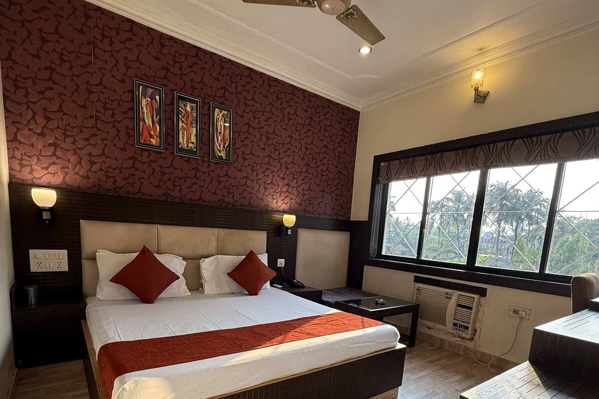 A spacious bedroom with a large bed, a ceiling fan, and a window with a view of greenery.
