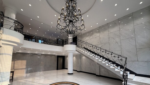 A spacious lobby with a grand staircase, a decorative chandelier, and a patterned floor. - Palm Village Resort (Alipur)