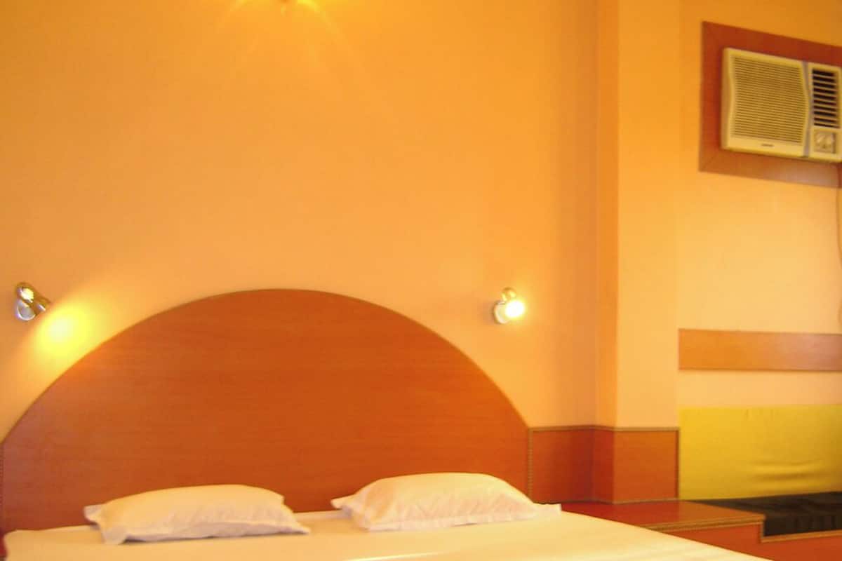 A hotel room with a large bed, two bedside lamps, and a wall-mounted air conditioning unit.
