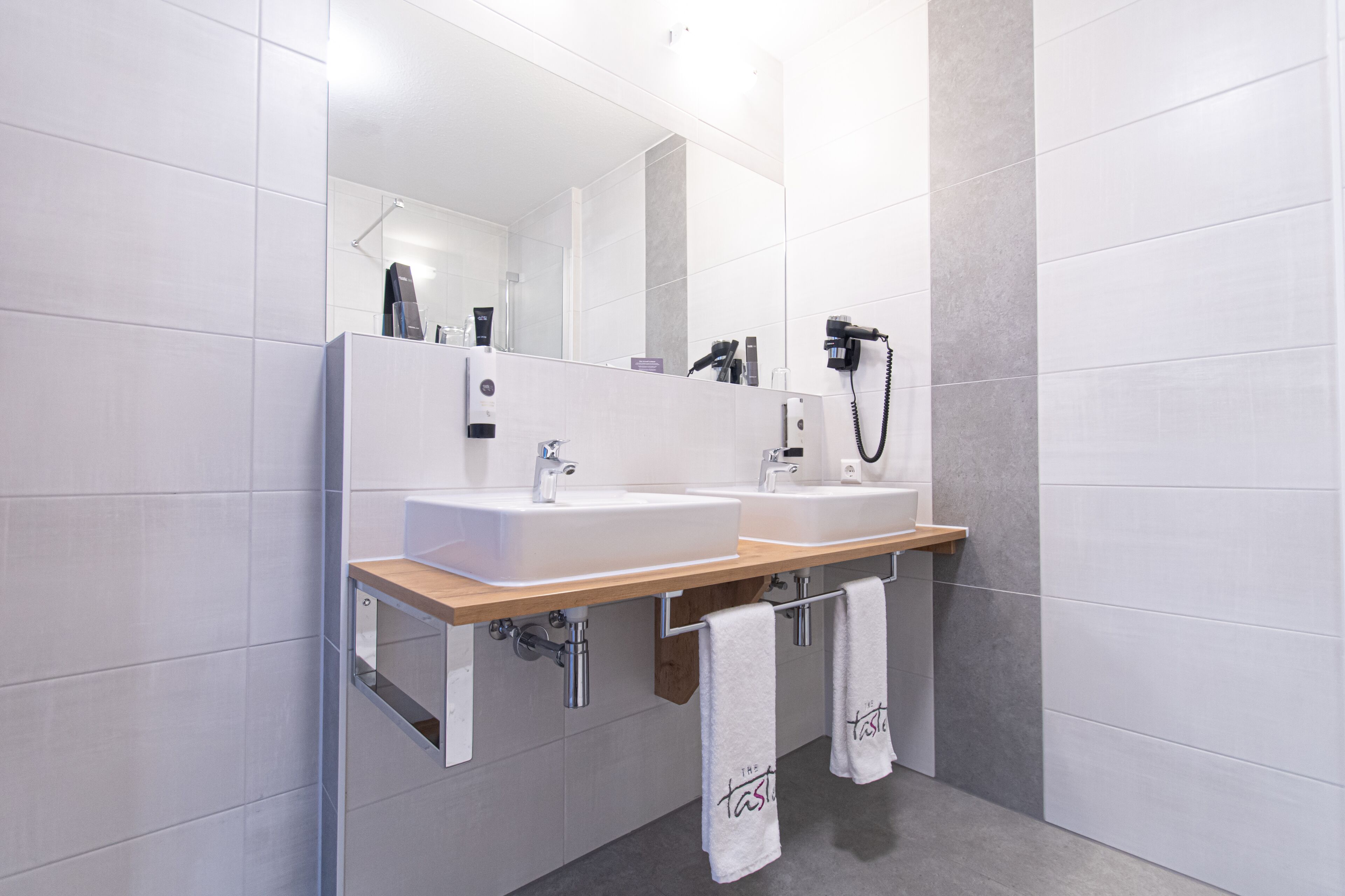 Un baño moderno con dos lavamanos, un espejo grande y un secador de pelo en la pared.