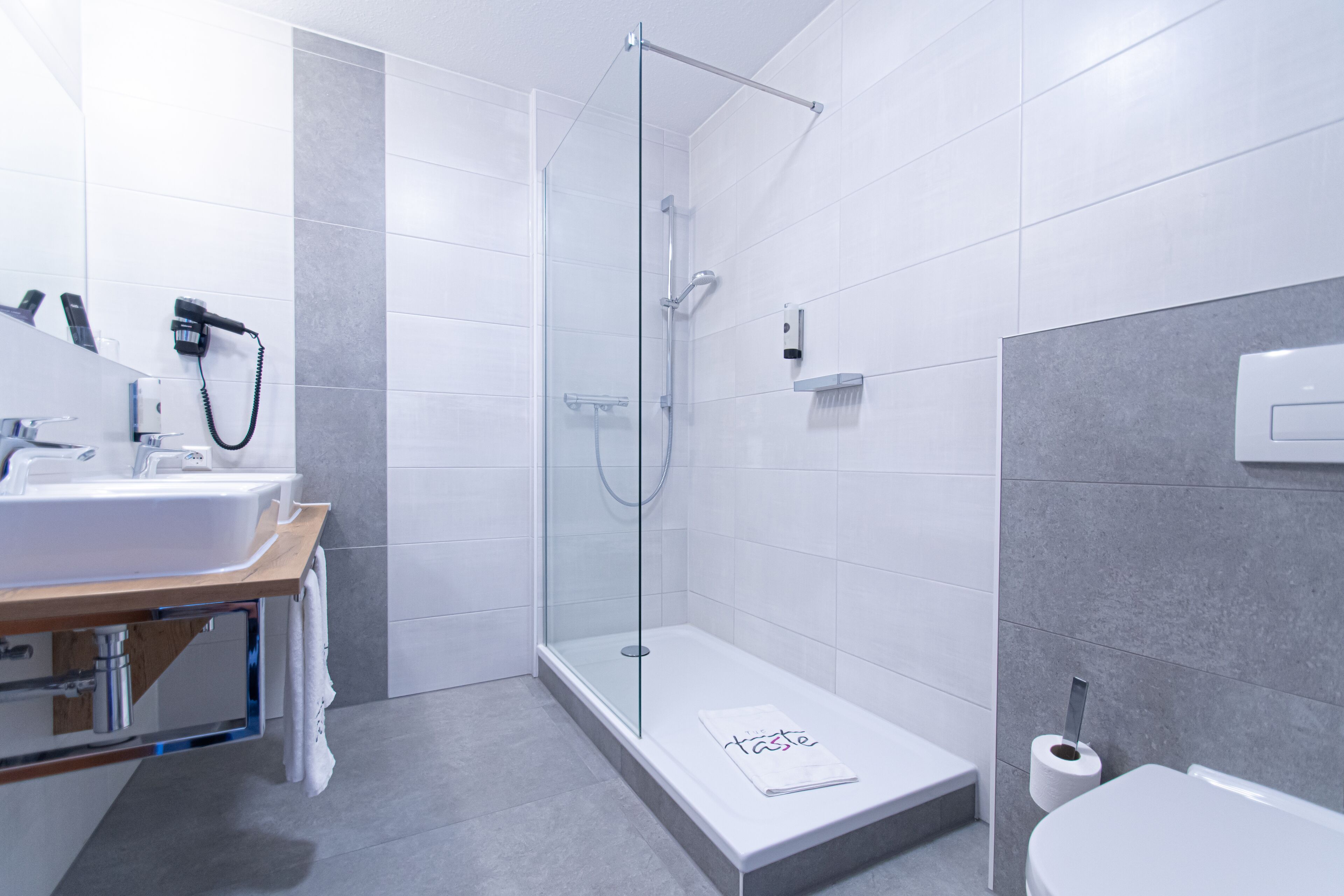 Un baño moderno con ducha de vidrio, lavamanos blanco y retrete.