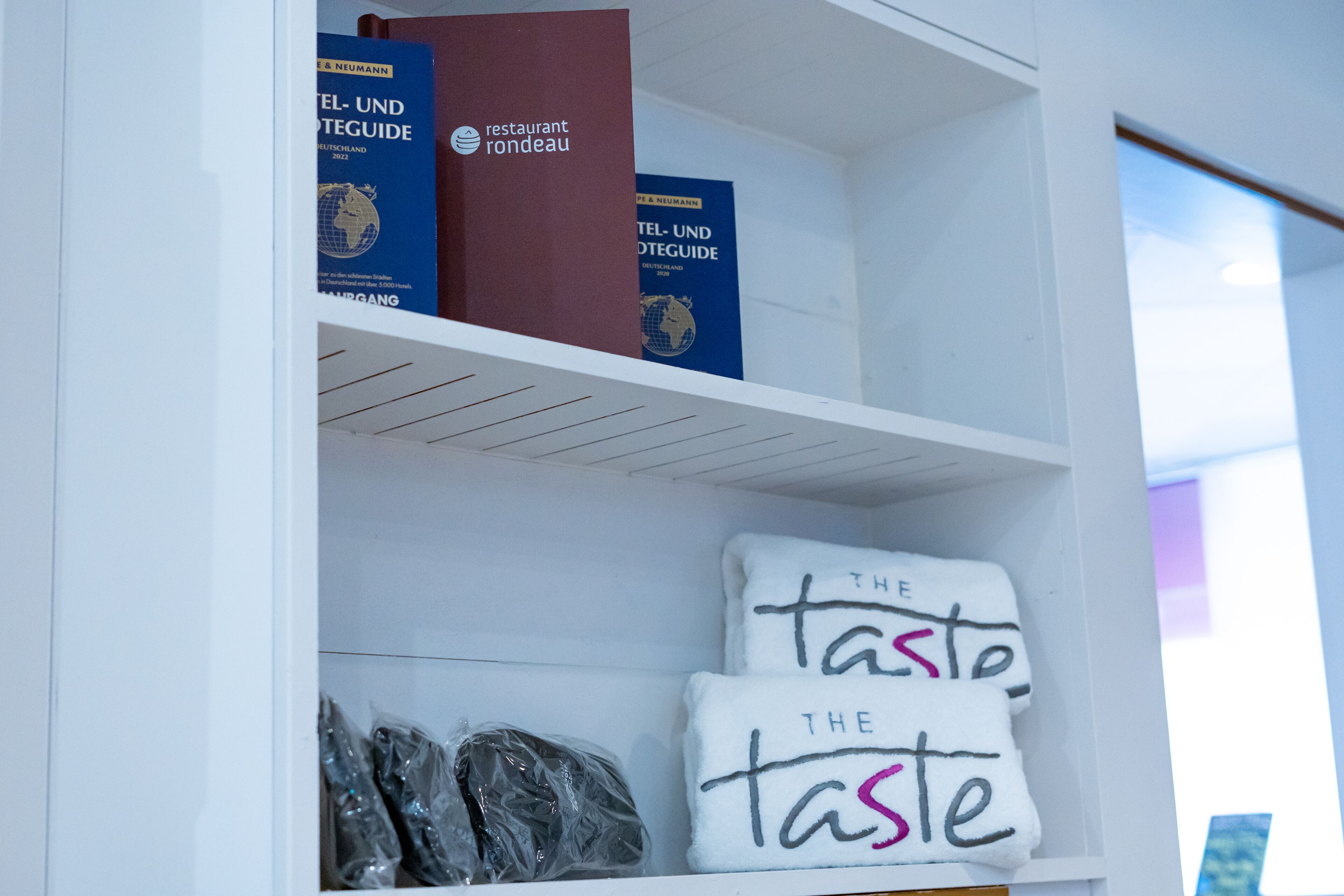 Un estante en un hotel con libros, toallas y bolsas de plástico.