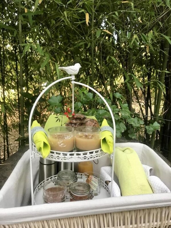 Una cesta de mimbre con un soporte de metal blanco que sostiene una figurina de pájaro, dos vasos de té helado y una servilleta amarilla.
