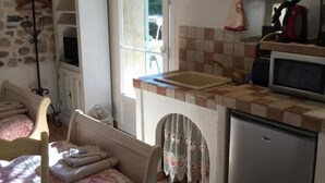 Eine kompakte Küche mit integriertem Spülbecken, Mikrowelle und Kühlschrank. Ein Fenster sorgt für natürliches Licht, und es gibt einen Essbereich mit Tisch und Stühlen.