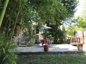 Eine Außenpatio mit Tisch und Stühlen, umgeben von Bambuspflanzen und einer Steinmauer.