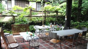 An outdoor patio area with tables and chairs, surrounded by lush greenery and a stone wall. - Miguel's Place at Canyon Woods Resort (Laurel)