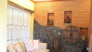 A cozy living room with a stone wall, a wooden chair, a sofa with floral cushions, and a small table with decorative items. - Miguel's Place at Canyon Woods Resort (Laurel)